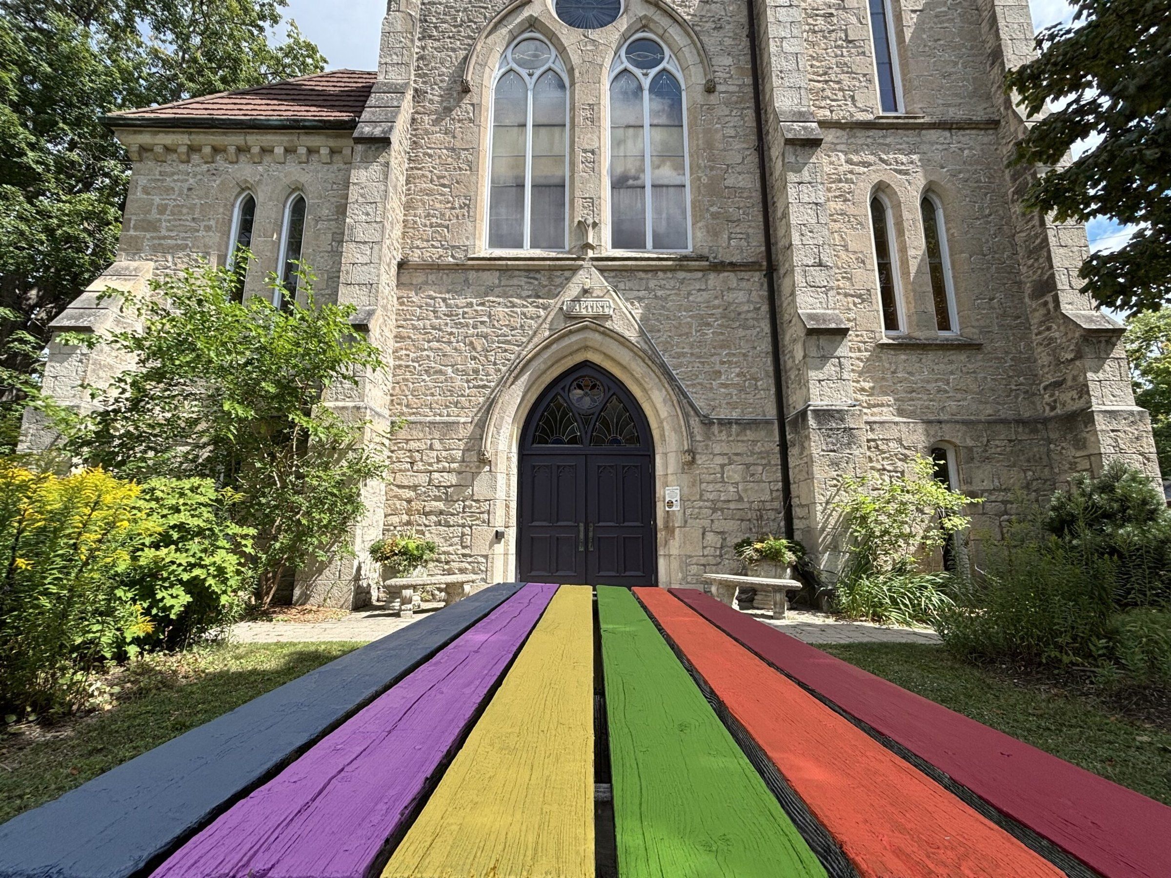 The stone front of First Baptist Church, with a rainbow-painted ramp leading to its arched door
